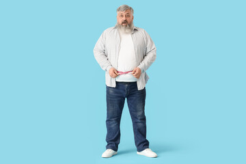Overweight mature shocked man with measuring tape on blue background. Weight loss concept