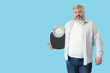 Overweight mature happy man with scales on blue background. Weight loss concept