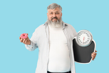 Overweight mature happy man with donut and scales on blue background. Weight loss concept