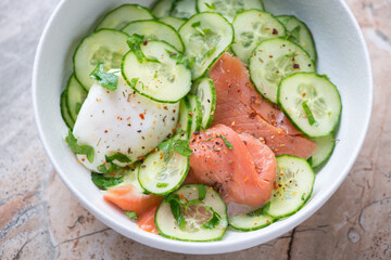 Cucumber salad with smoked salmon and poached egg in a white bowl, horizontal shot, middle closeup,...