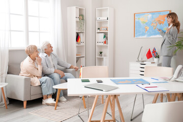 Female travel agent showing mature couple world map in office