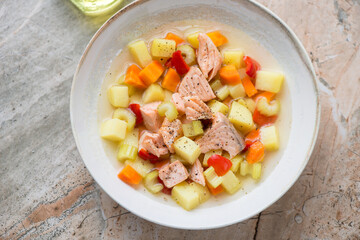 Beige plate with salmon and vegetable soup, horizontal shot on a grey and roseate granite surface, high angle view