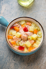 Vegetable soup with salmon in a turquoise serving bowl, vertical shot on a light-brown granite background, elevated view