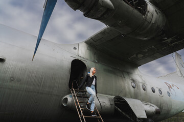 A blonde girl descends the ramp from an old decommissioned Soviet military cargo plane An-12.