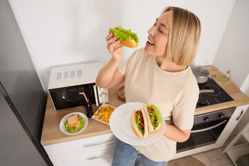 Beautiful woman with tasty hot dogs in kitchen. Overeating concept