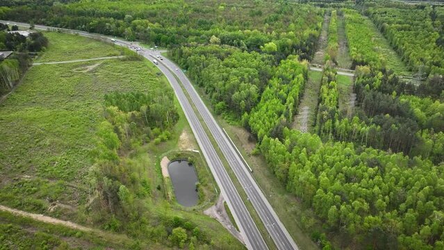 Aerial footage of national road with traffic lights, vehicles and traffic, a power line runs nearby, as camera tilts up, it reveals coal-fired power plant with cooling towers from which smoke emerges.