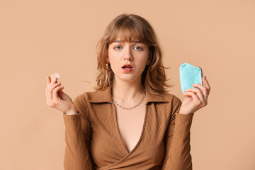 Sad young woman holding blue purse and coins on brown background