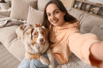 Young woman with cute fluffy Australian Shepherd dog taking selfie in living room