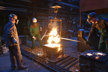 Group of workers in an iron foundry - casting a workpiece with liquid hot metal into a mold - cooperation and work safety