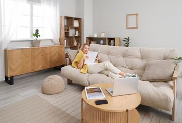 Young woman reading magazine on sofa in stylish living room