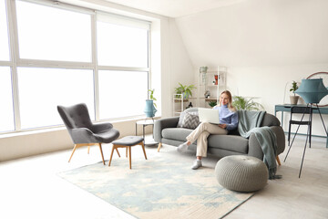 Young woman using laptop and sitting on sofa in white living room
