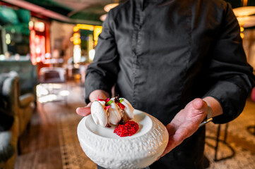 A chef elegantly presents a dessert adorned with red berries in a restaurant setting