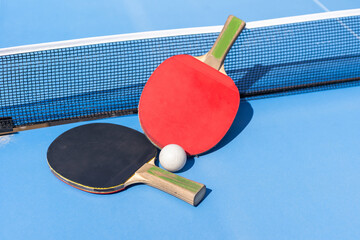 Two table tennis or ping pong rackets and ball on blue table with net