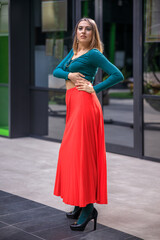 A young woman in bright clothes, a red skirt and a green longsleeve is standing in a business center. High-heeled shoes.