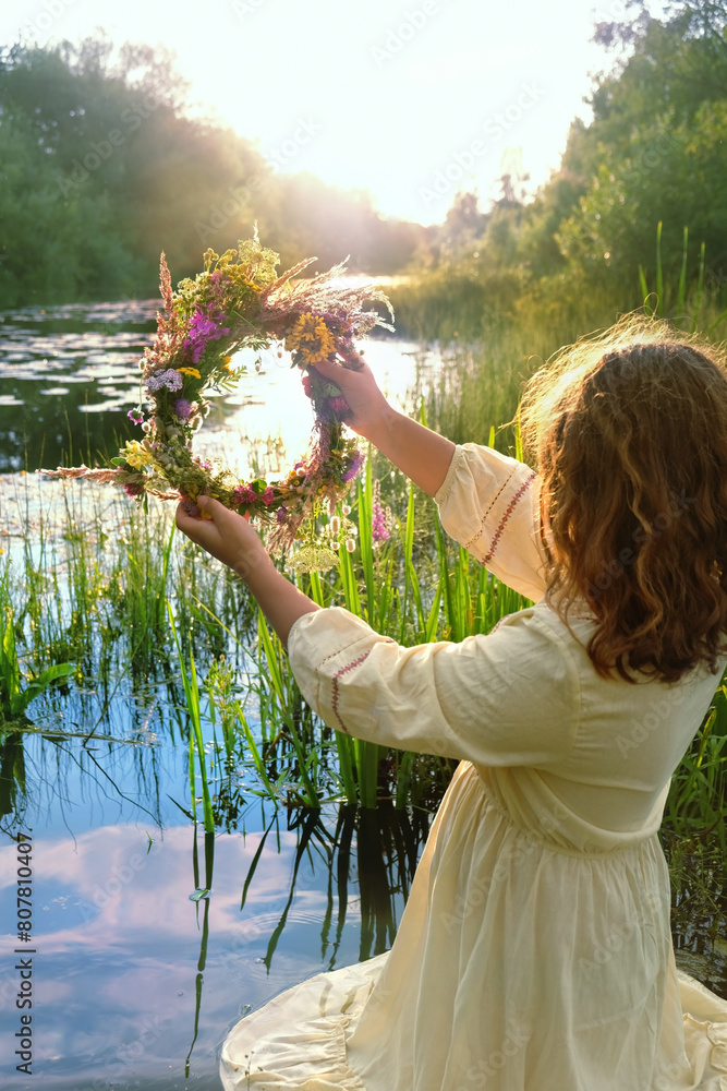 Wall mural girl with flower wreath stand in river. summer nature background. floral crown, symbol of summer sol