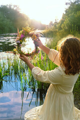 girl with flower wreath stand in river. summer nature background. Floral crown, symbol of summer...