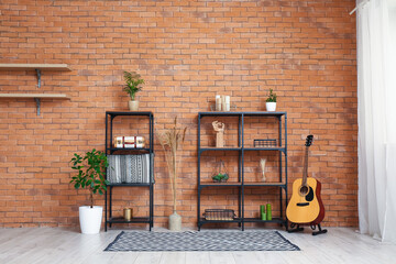 Shelving units, guitar and houseplants near brown brick wall in stylish room