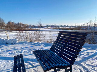 Une banc sur une promenade enneigée le long d'une rivière gelée avec des roseaux, et au loin, on...