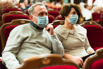 Elderly couple in antivirus mask watching play in the theater