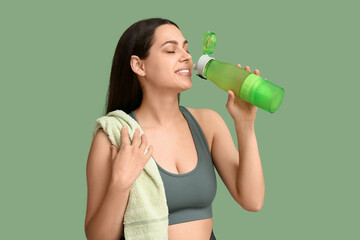 Beautiful young happy woman with towel and sports bottle of water on green background