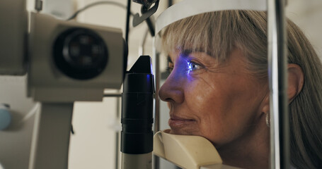Mature woman, slit lamp and face for eye test or medical service with optometry technology. Eyeball, led light or patient with assessment for healthcare with lens for vision and ophthalmology