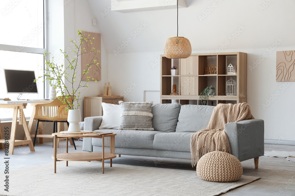 Wall mural Interior of stylish living room with sofa, coffee table, workplace and blooming tree branches in vase