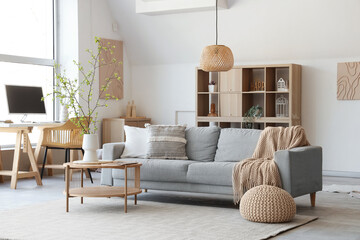 Interior of stylish living room with sofa, coffee table, workplace and blooming tree branches in vase
