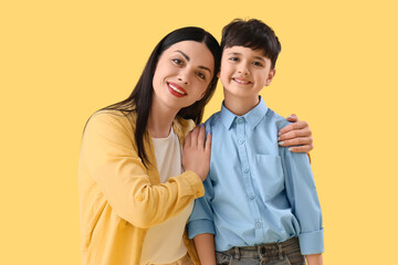 Mother hugging her little son on yellow background