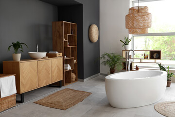 Interior of modern bathroom with bathtub, wooden furniture and houseplants