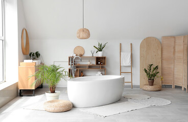Interior of light bathroom with ceramic bathtub and houseplants