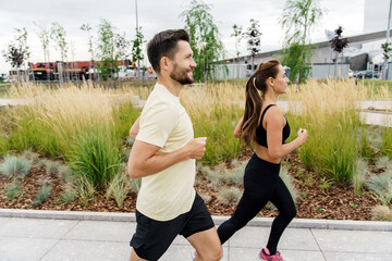 A dynamic image capturing couple running side-by-side in an urban park, highlighted by lush grass...