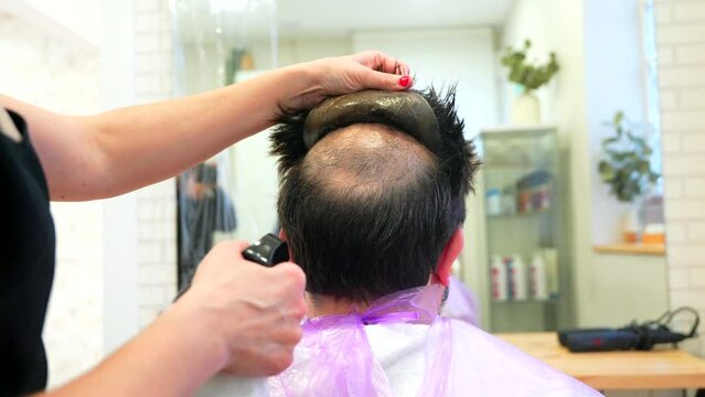 Close-up photo of the hands of a hairstylist removing the capillary prosthesis of a man in the hair salon