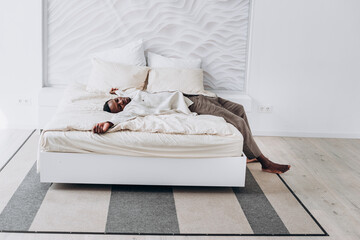 African American man enjoys a peaceful sleep in modern, minimalist bedroom, featuring white bed on patterned rug and uniquely textured wall.
