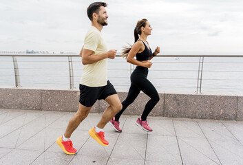 A dynamic image of a fit couple energetically jogging along a seaside promenade, with a scenic...