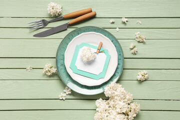 Beautiful table setting with white lilac flowers and invitation on green wooden background