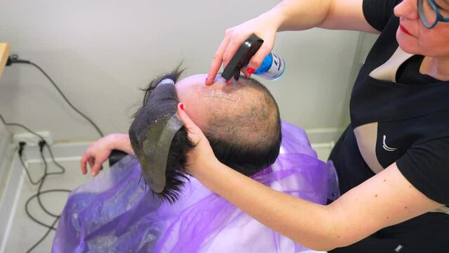 Side view of a friendly hairdresser removing carefully the capillary prosthesis to a client