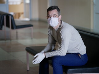 Man wearing protective gloves on hands and mask on face nervously impatiently waiting in the lobby