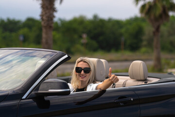 Close-up of a young smiling blonde woman in sunglasses at the wheel of a convertible convertible...