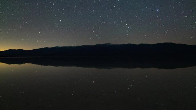 Timelapse pan shot of starry sky reflected in ancient Lake Manly at Badwater Basin in Death Valley National Park in California, USA
