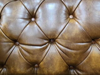 Golden brown upholstery artificial leather with rivets for sofa or bed. Vintage genuine leather Sofa.  Leather chesterfield brown pattern detail. luxurious sofa. 
