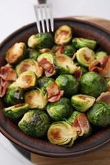 Delicious roasted Brussels sprouts and bacon in bowl on table, closeup