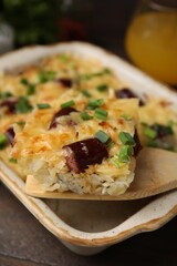 Taking piece of tasty sausage casserole from baking dish at table, closeup