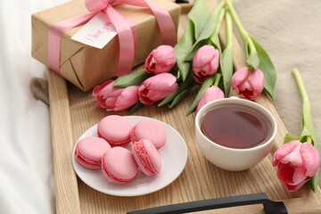 Tasty breakfast served in bed. Delicious macarons, tea, flowers, gift box and card with phrase I Love You on tray