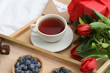 Tasty breakfast served in bed. Delicious tartlets, tea, flowers and card with phrase Love You on tray