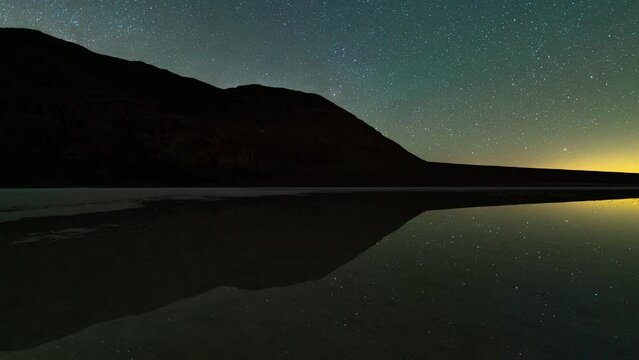 Timelapse night to day tracking shot of Milky Way galaxy reflected in ancient Lake Manly at Badwater Basin in Death Valley National Park in California, USA