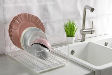 Drainer with different clean dishware on white table in kitchen