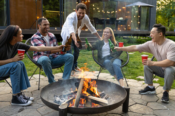 Cheerful multicultural friends sitting near fire on backyard enjoying happy weekend