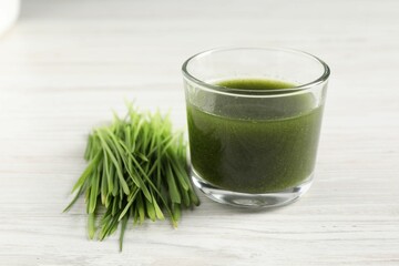 Wheat grass drink in glass and fresh sprouts on white wooden table, closeup