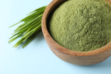Wheat grass powder in bowl and fresh sprouts on light blue background, closeup