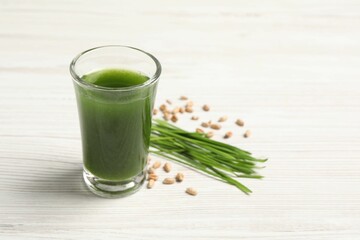 Wheat grass drink in shot glass, seeds and fresh green sprouts on white wooden table, closeup